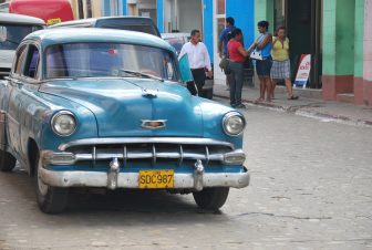 a classic car and people on the road in Trinidad in Cuba